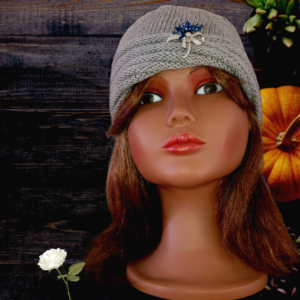 Tricot fait mainUn bonnet bleu nuit en forme de turban, tricoté avec une laine mérinos extrafine, et décoré d’une broche blanche en forme de fleur sur le devant.