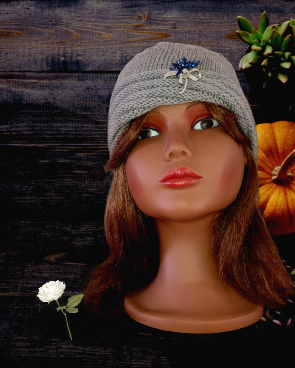 Tricot fait mainUn bonnet bleu nuit en forme de turban, tricoté avec une laine mérinos extrafine, et décoré d’une broche blanche en forme de fleur sur le devant.
