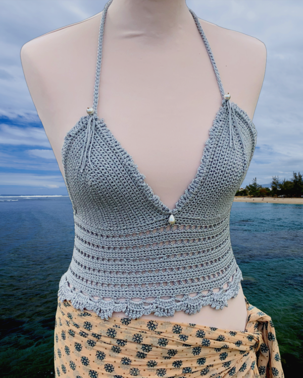 Un bustier gris crocheté avec des motifs variés et des perles grises. Le bustier a des bretelles nouées au cou et une lanière au dos