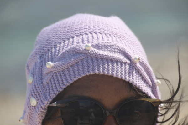Un bonnet en laine lilas avec une bordure torsadée et des perles blanches sur le devant et deux perles sur l'arrière