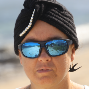Une femme souriante porte un turban gris en cachemire tricoté main avec des perles sur le devant