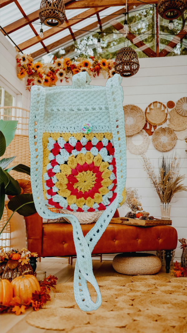 “Pochette granny square crochetée main en coton recyclé blanc cassé, rouge et jaune tournesol, avec bandoulière de 120 cm et fermeture par bouton en bois naturel.”