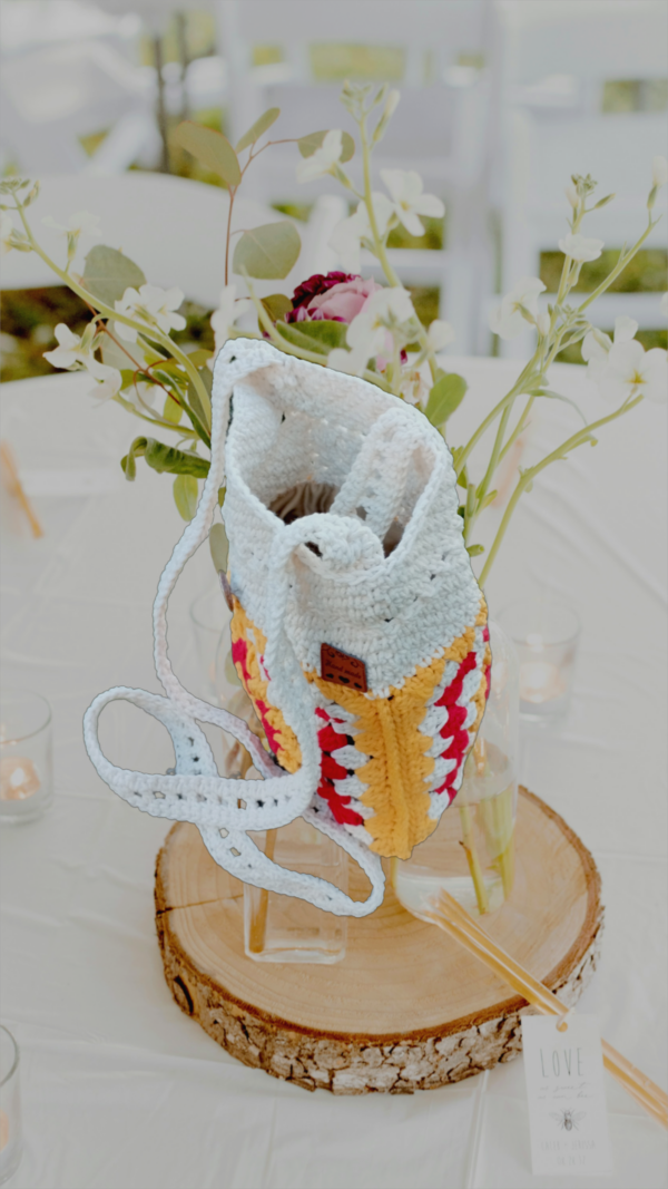 “Pochette granny square crochetée main en coton recyclé blanc cassé, rouge et jaune tournesol, avec bandoulière de 120 cm et fermeture par bouton en bois naturel.”