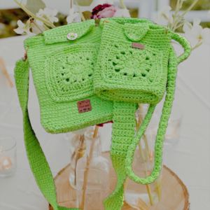 “Pochette téléphone et porte-cartes crochetée en coton recyclé de couleur anis, avec motifs granny, mailles serrées et mailles coulées. Lanière généreuse pour plus de confort.”