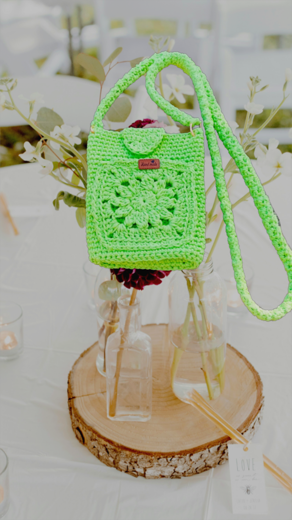 “Pochette téléphone et porte-cartes crochetée en coton recyclé de couleur anis, avec motifs granny, mailles serrées et mailles coulées. Lanière généreuse pour plus de confort.”