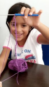 Enfants souriants apprenant le crochet dans une ambiance conviviale.