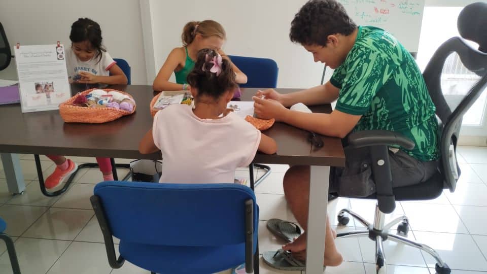Enfants souriants apprenant le crochet dans une ambiance conviviale.