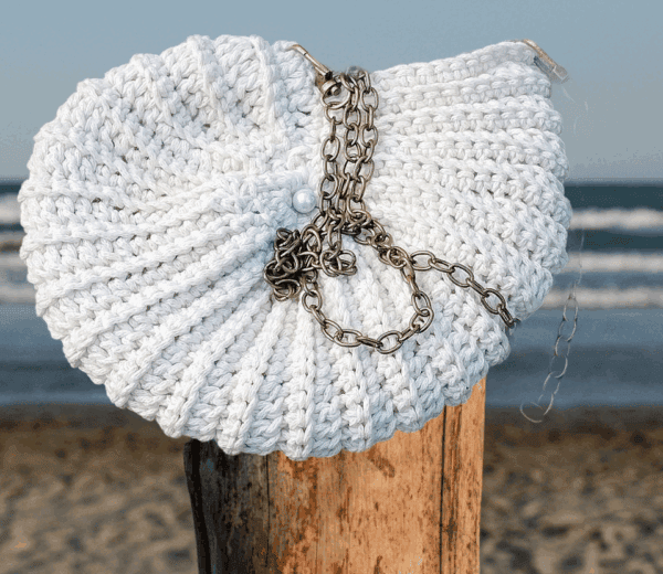 Sac crocheté à la main en coton recyclé, forme inspirée des coquillages, avec une chaîne en métal et une perle nacrée en ornement.
