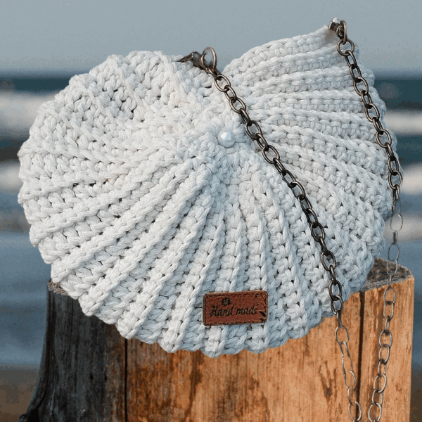 Sac crocheté à la main en coton recyclé, forme inspirée des coquillages, avec une chaîne en métal et une perle nacrée en ornement.