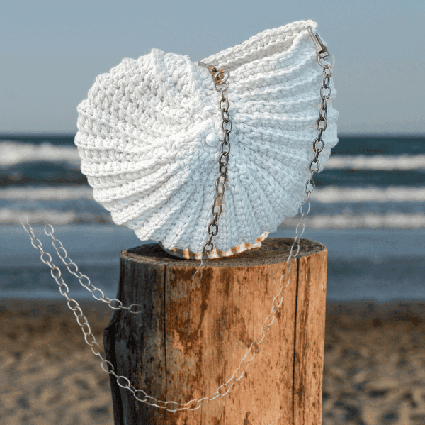 Sac crocheté à la main en coton recyclé, forme inspirée des coquillages, avec une chaîne en métal et une perle nacrée en ornement.