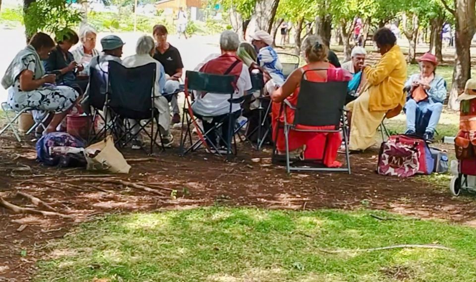 "Des Seniors réunis au Parc de la Trinité pour un atelier tricot et crochet en plein air. Chaises, tapis et pelotes colorées témoignent d’une ambiance conviviale et chaleureuse."
